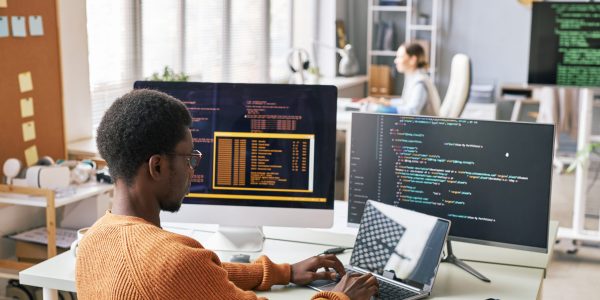Young man in warm sweater coding on laptop in office of IT company
