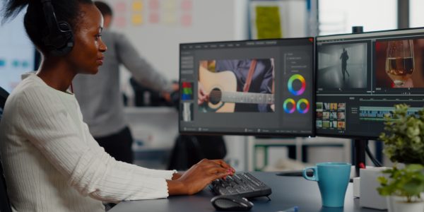 Black woman video editor editing new project film montage sitting in modern creative agency office. Content creator in digital multimedia company processing movie with post production software