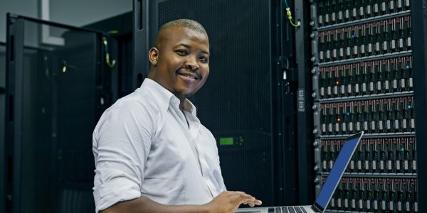 Server room, black man or portrait of technician with laptop for online cyber security glitch or software. IT support, happy or friendly African engineer fixing network for information technology.